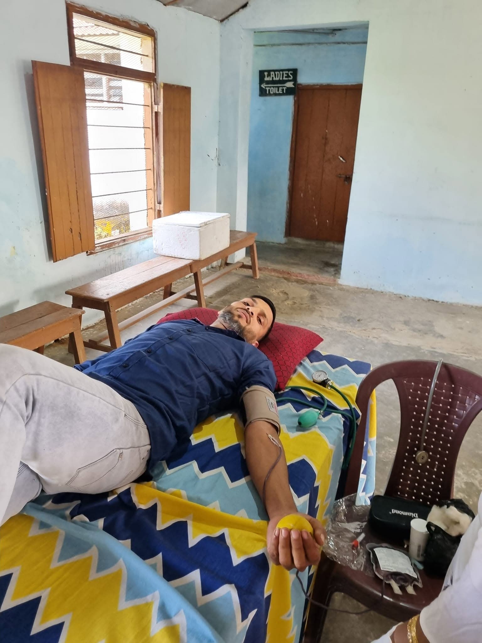 A man lying on a medical bed donating blood during a supervised community blood camp.