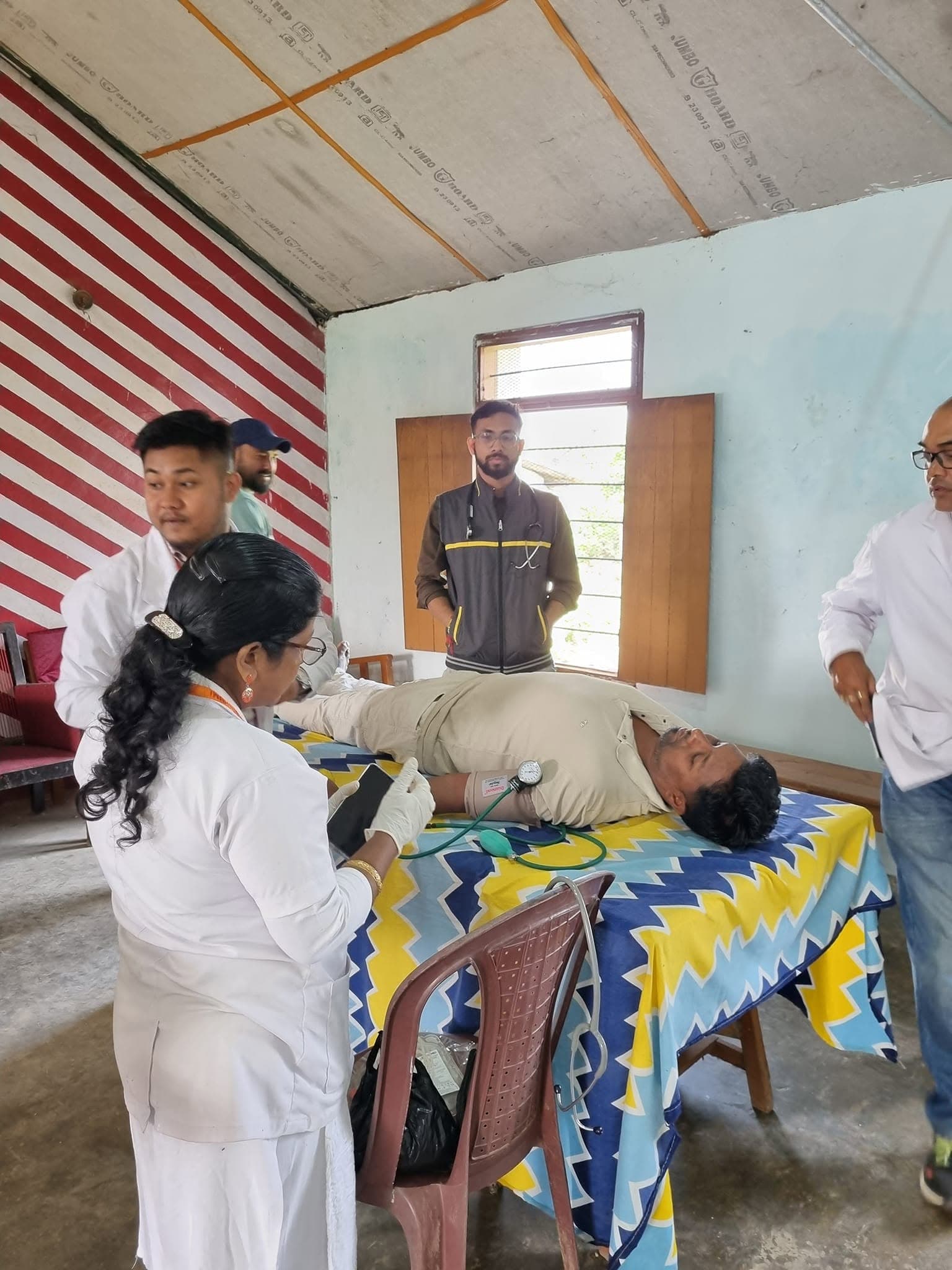 Healthcare worker taking blood pressure of a patient on a bed in a rural medical setup.