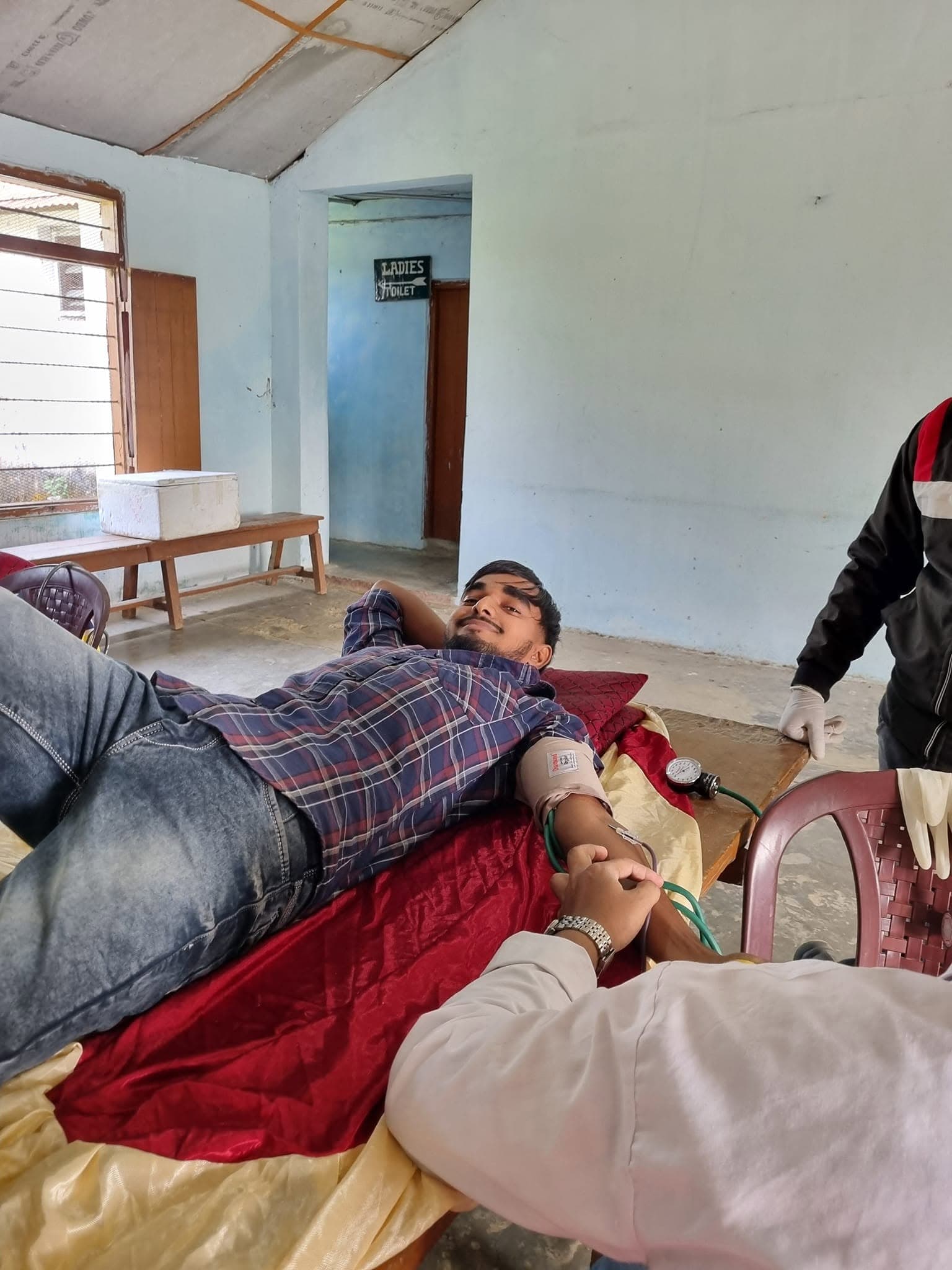 Volunteer assisting a donor lying on a medical bed during a blood collection drive.