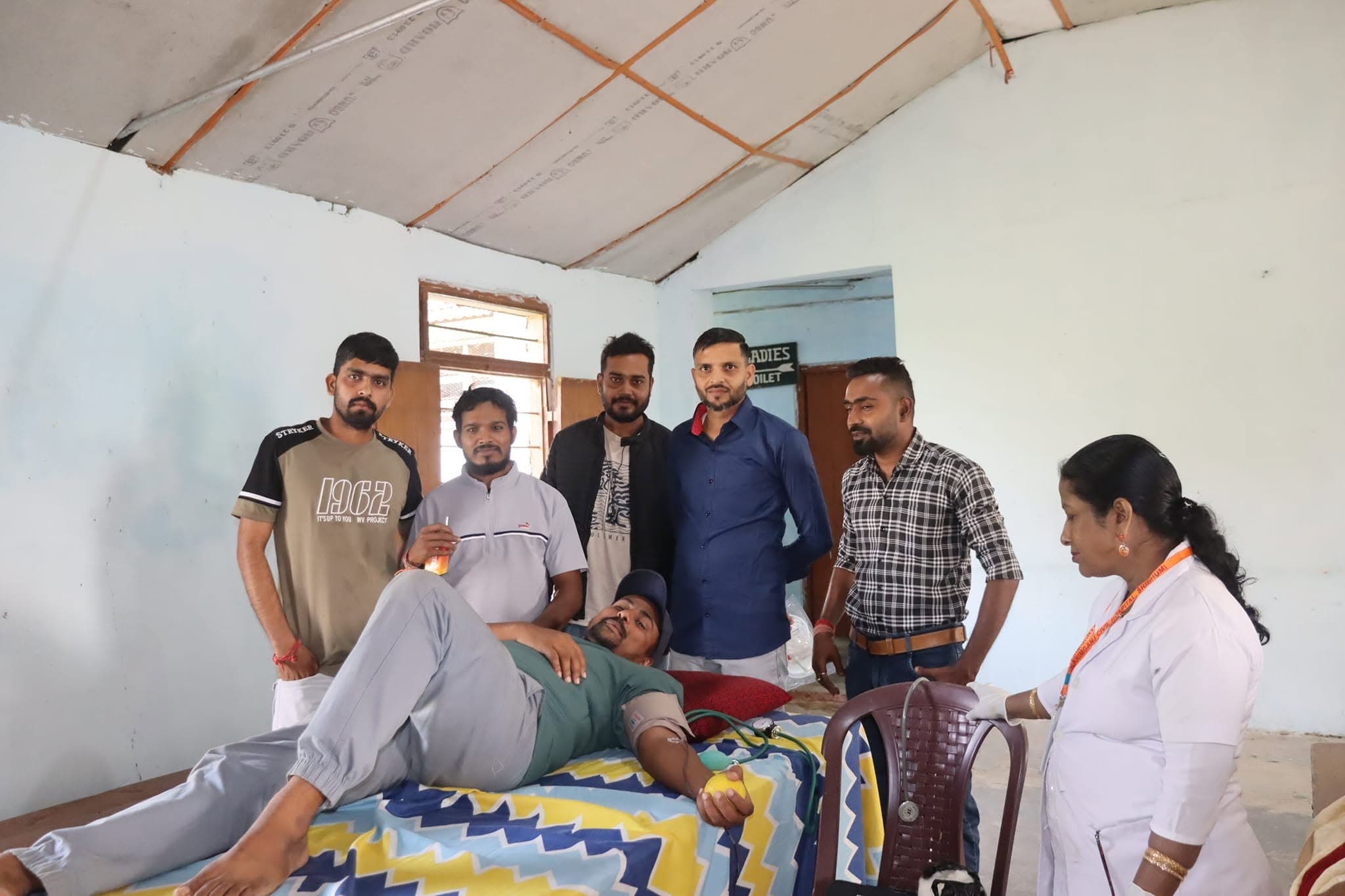 Volunteers and healthcare staff standing around a donor bed in a health camp facility.