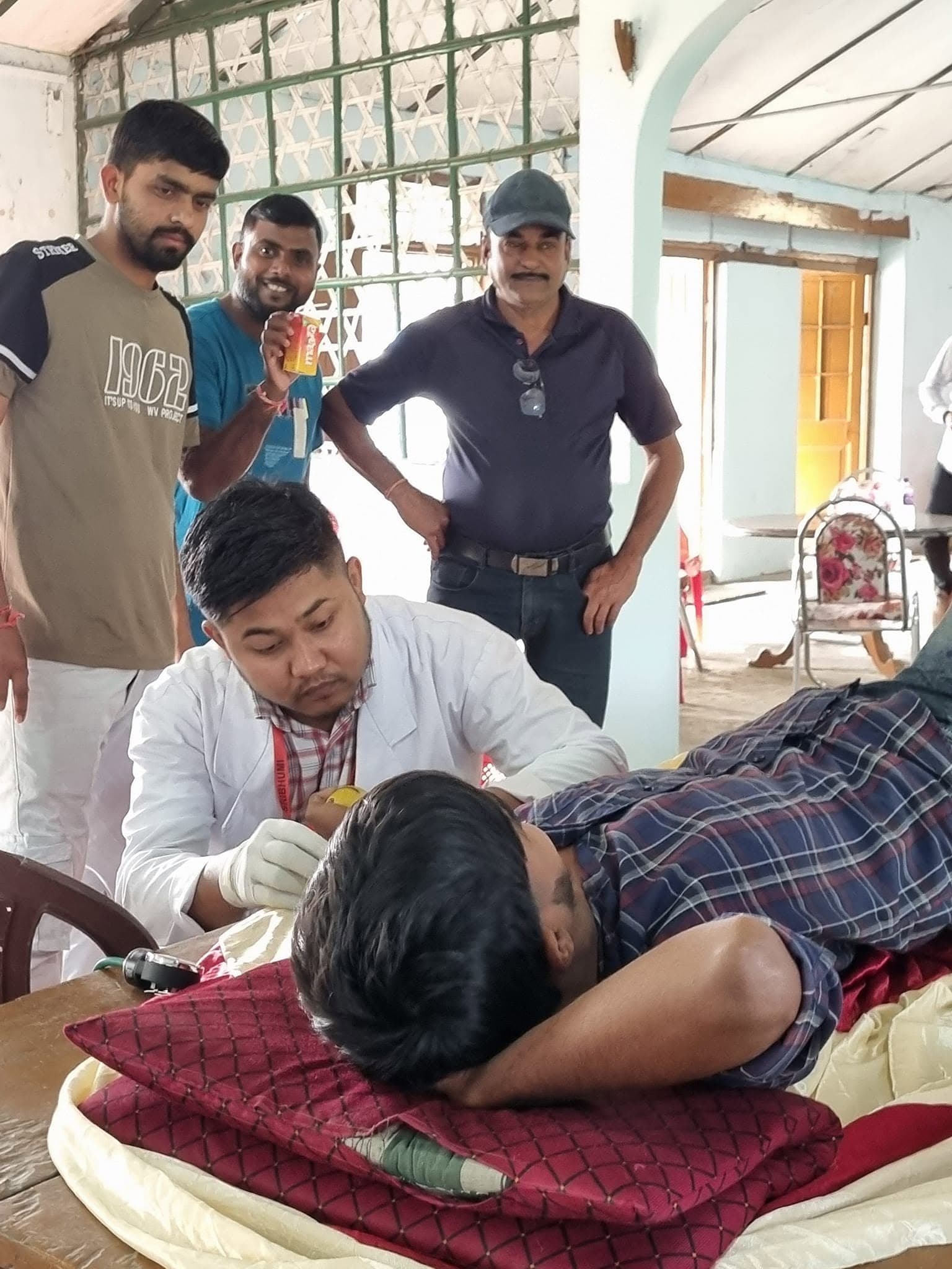 Volunteers and healthcare worker attending to a resting donor with refreshment in hand.