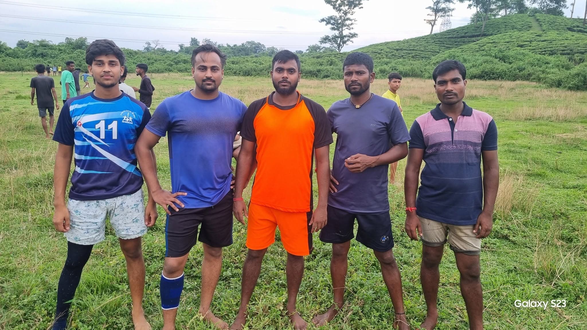 Five young local volunteers in sportswear standing in a green tea garden meadow.